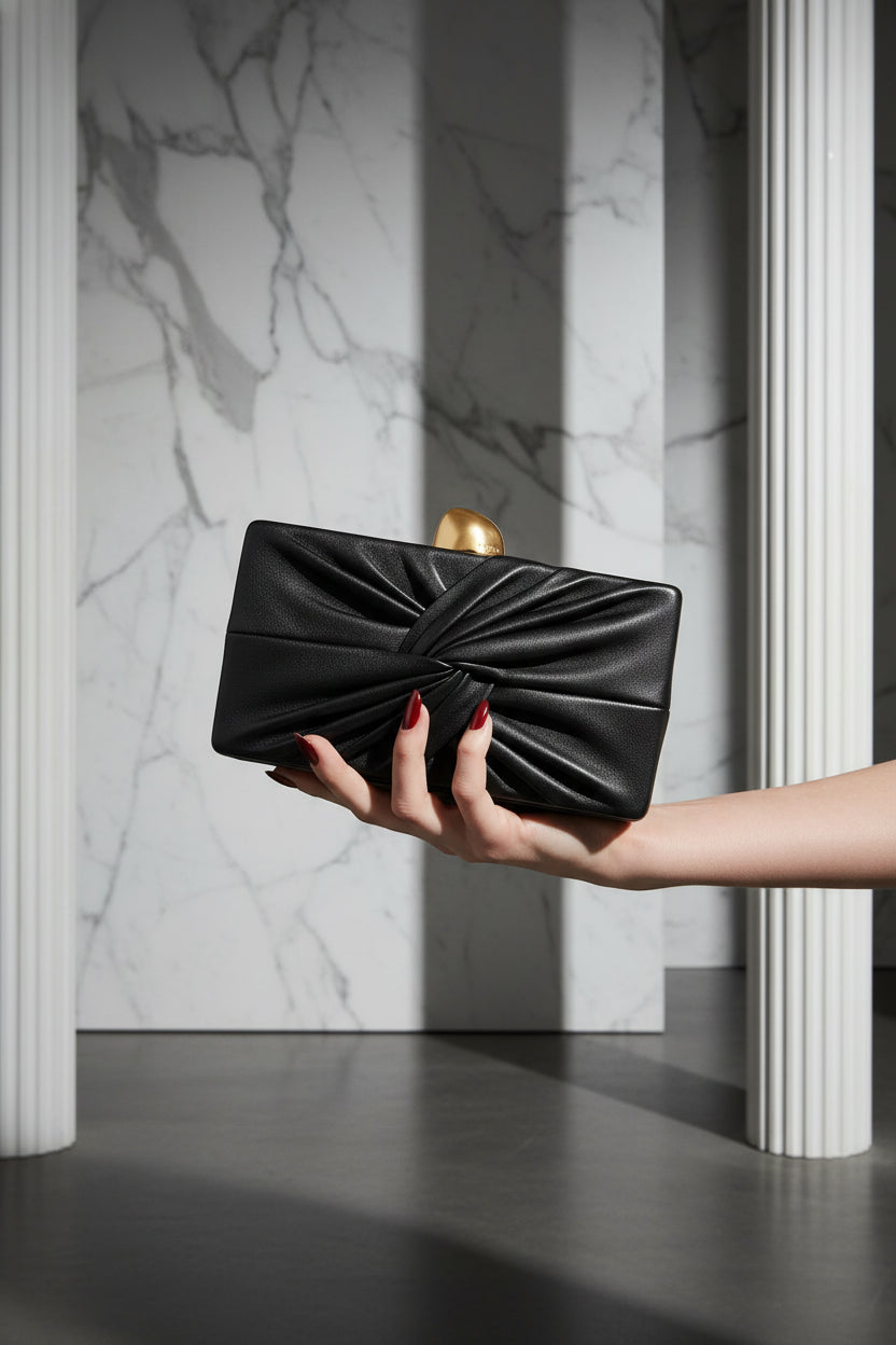 Black clutch bag with a gold clasp on a beige background