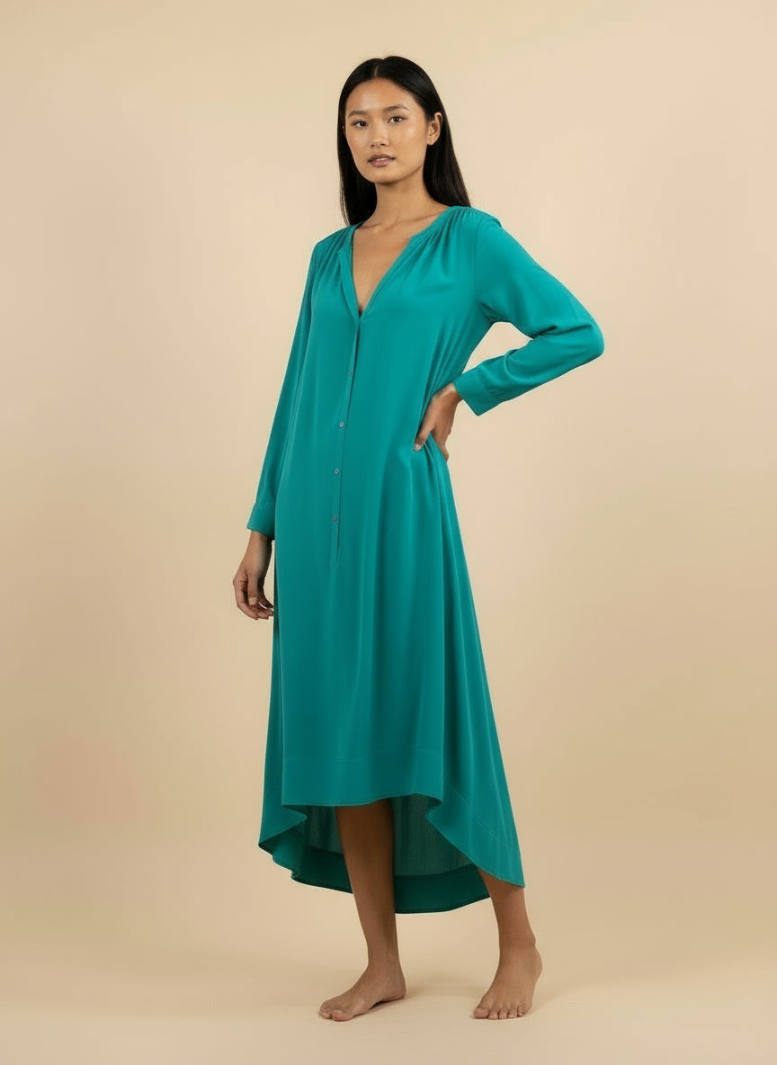 A woman wearing a turquoise viscose dress with a round neckline, long sleeves.